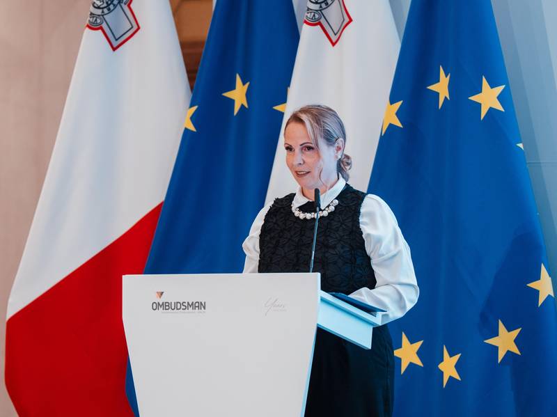 Namestnica varuha dr. Dijana Možina Zupanc za govorniškim pultom. V ozadju so zastave.